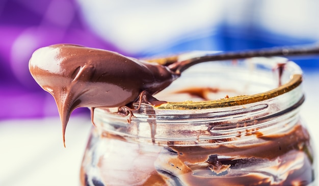 Foto chocolate para untar en cuchara. un tarro de crema de chocolate con avellanas.