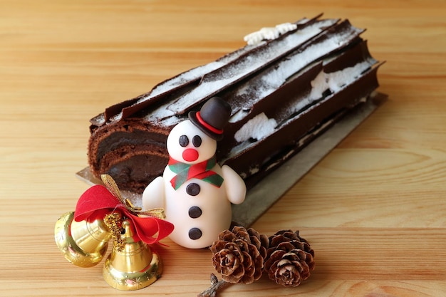 Chocolate Yule Log Cake o Buche de Noel con mazapán de muñeco de nieve y adorno navideño en mesa de madera