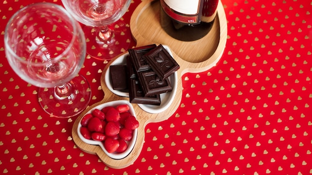 Chocolates e doces em pratos em forma de coração. Configuração de mesa festiva para data de namorados. Fundo vermelho