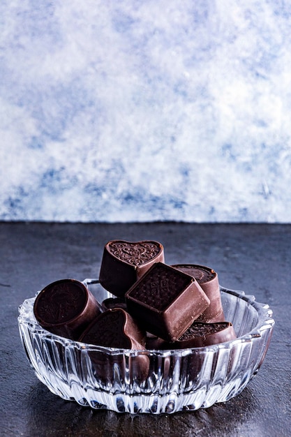 Chocolates em bandeja de vidro esculpida, fotografados em um fundo escuro.