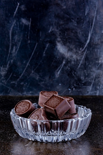 Chocolates em bandeja de vidro esculpida, fotografados em um fundo escuro.