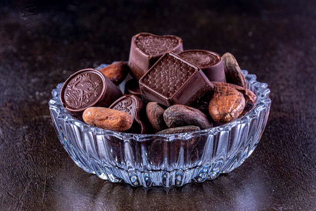 Chocolates em bandeja de vidro esculpida, fotografados em um fundo escuro.