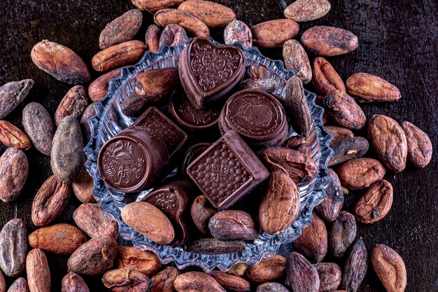 Chocolates em bandeja de vidro esculpida, fotografados em um fundo escuro.