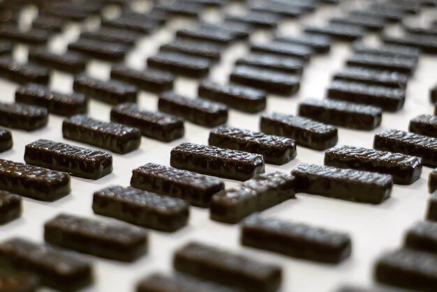 Chocolates recién vertidos con chocolate líquido sobre una cinta transportadora de cerca de una fábrica de confitería