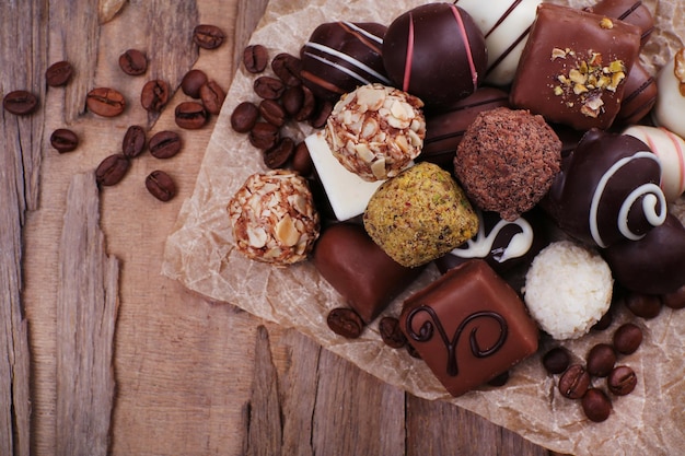 Chocolates surtidos en papel desmoronado con granos de café sobre fondo rústico de madera