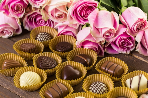 Chocolates surtidos con rosas rosadas en mesa de madera.