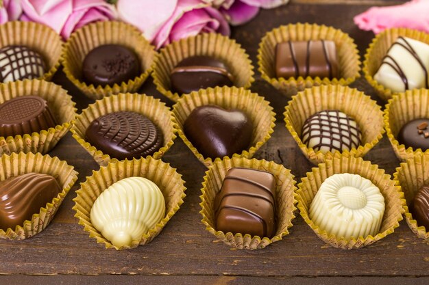 Chocolates surtidos con rosas rosadas en mesa de madera.