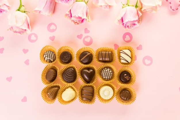 Chocolates surtidos con rosas rosadas sobre fondo rosa.