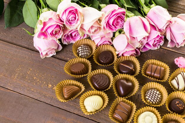 Chocolates variados com rosas cor de rosa na mesa de madeira.