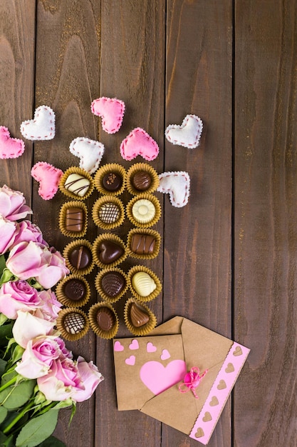 Chocolates variados com rosas cor de rosa na mesa de madeira.