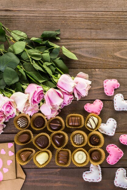 Chocolates variados com rosas cor de rosa na mesa de madeira.