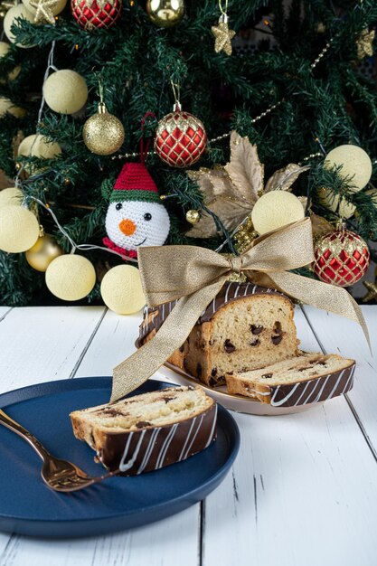 Chocotone com um laço de fita perto da árvore de Natal Na fatia de primeiro plano desfocada de Chocotone