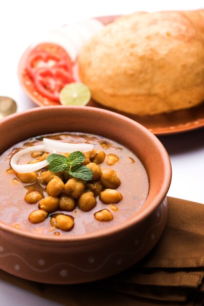 Chole Bhature o curry de garbanzos y Puri frito servido en vajilla de terracota sobre fondo blanco. enfoque selectivo