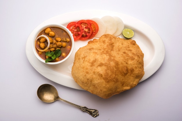 Chole Bhature o curry de garbanzos y Puri frito servido en vajilla de terracota sobre fondo blanco. enfoque selectivo