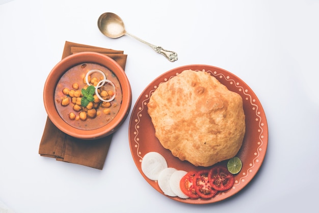 Chole Bhature oder Kichererbsen-Curry und Fried Puri serviert in Terrakotta-Geschirr auf weißem Hintergrund. selektiver Fokus