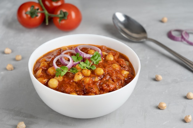 Chole masala o comida india chana hecha de garbanzos y tomates con cebolla en mesa de hormigón gris