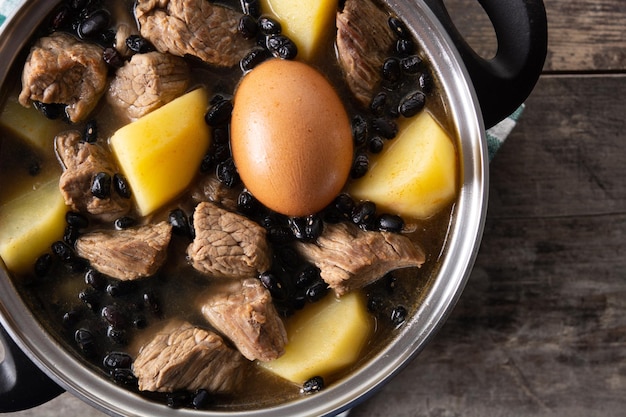 Cholent judío tradicional en cazuela sobre mesa de madera