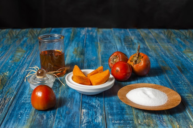 Chontaduro, frutas tropicais exóticas, cortadas com sal e mel ao lado de chontaduros crus em uma mesa de madeira azul rústica. Bactris gasipas
