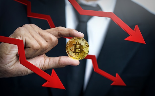 Choque de precios de Bitcoin. Empresario sosteniendo Bitcoin con flecha roja 3D hacia abajo