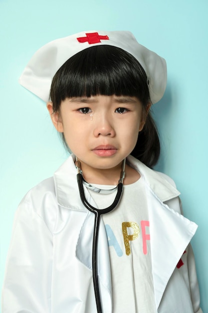 Chorando menina asiática em uniforme médico com estetoscópio