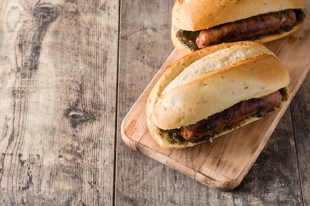 Choripan. Sanduíche tradicional da Argentina com molho de chouriço e chimichurri na mesa de madeira