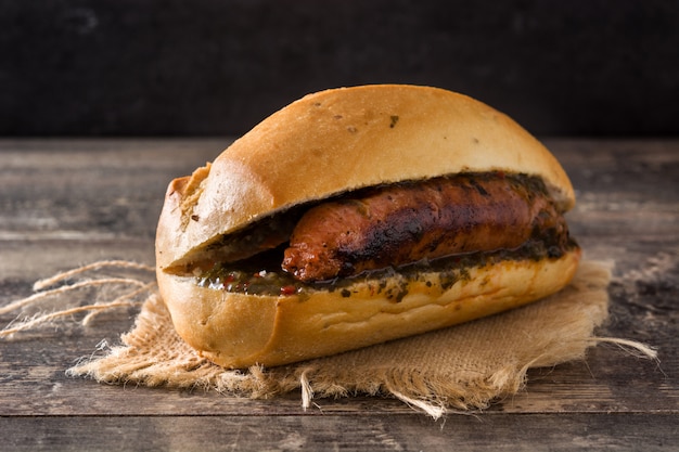 Choripan. Sanduíche tradicional da Argentina com molho de chouriço e chimichurri na mesa de madeira