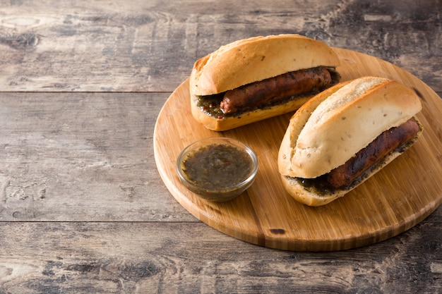 Choripan. Traditionelles Argentinien-Sandwich mit Chorizo und Chimichurri sauce auf Holztisch