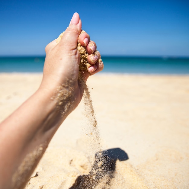 Un chorro de arena cae de la mano de una mujer en una playa de arena