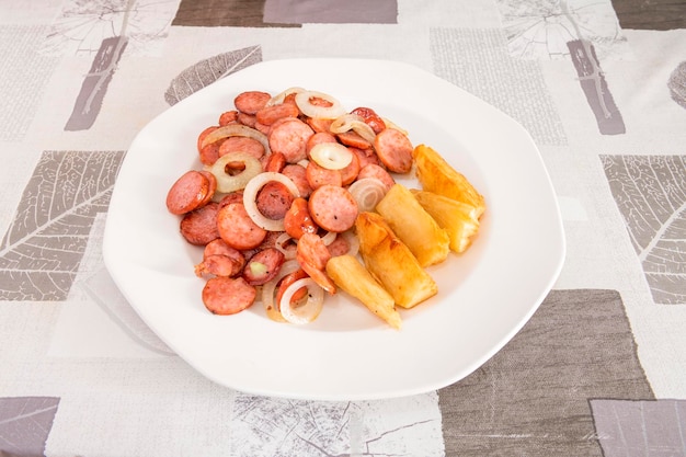 Foto chouriço defumado picado e frito com rodelas de cebola branca e deliciosa mandioca frita