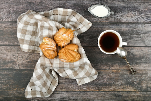 Choux-kuchen mit kaffee auf einem holz. in einem korb auf einem karierten handtuch. . schick mit quark. kleine vanillepuddingkuchen in weidenschale auf holz