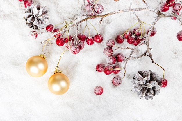 Christbaumkugeln auf einem Ast mit roten Beeren und Tannenzapfen