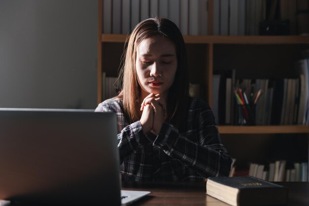 Christian concepto de tecnología en línea manos orando de cristiano con computadora digital portátil iglesia en línea en vivo para el servicio dominical hombre católico asiático están leyendo la Biblia libro y estudio en línea