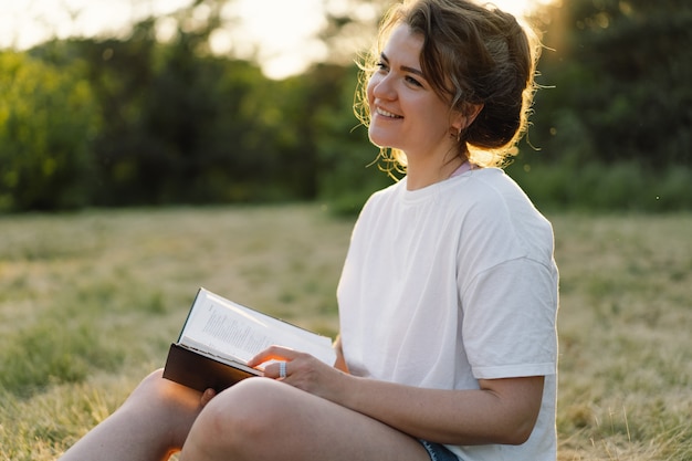 Christliche Frau hält Bibel in ihren Händen und liest die Bibel auf einem Feld während des schönen Sonnenuntergangs