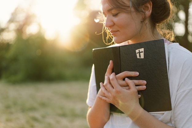 Christliche Frau hält Bibel in ihren Händen und liest die Bibel auf einem Feld während des schönen Sonnenuntergangs