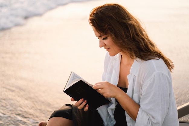 Christliche Frau hält Bibel in ihren Händen und liest die heilige Bibel auf dem Meer während des schönen Sonnenuntergangs