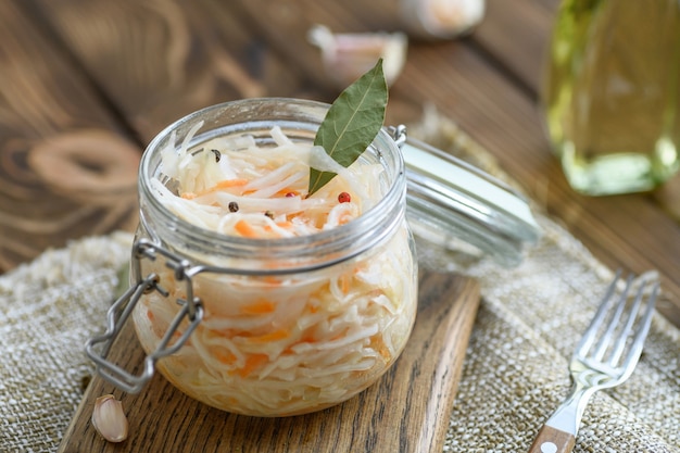 Chucrut agrio en escabeche con zanahorias y hojas de laurel en un frasco de vidrio.