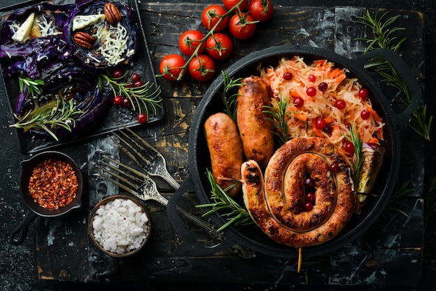 Chucrut y salchichas a la parrilla con romero y arándanos en un plato negro Plato tradicional alemán Vista superior Sobre un fondo de piedra negra