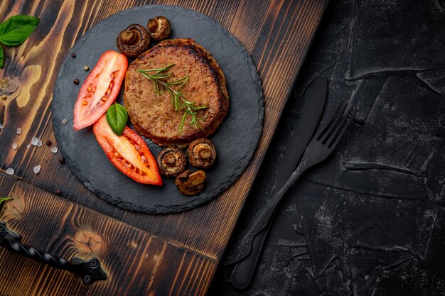Chuleta de carne con champiñones y romero sobre una placa de pizarra y un fondo negro. Espacio libre para su texto. Foto de alta calidad