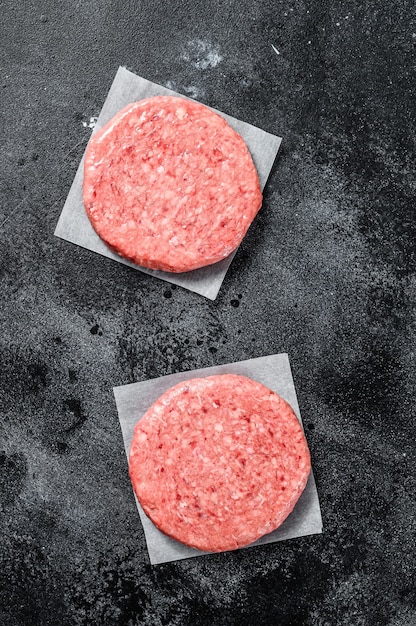 Foto chuleta de carne molida cruda, carne picada. empanadas de hamburguesa. fondo negro. vista superior.