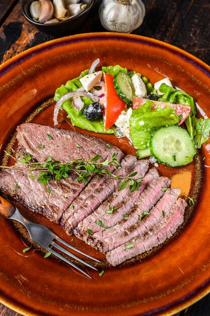 Chuleta de carne de ternera a la parrilla bistec redondo en un plato con ensalada. Mesa de madera oscura. Vista superior.