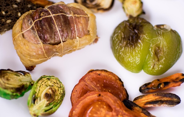 Chuleta de carne con verduras asadas en un plato blanco y sobre un fondo oscuro