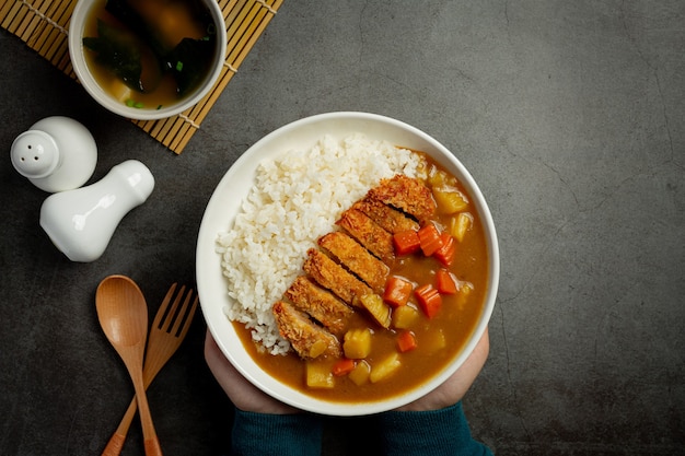 Chuleta de cerdo frita al curry con arroz sobre superficie oscura