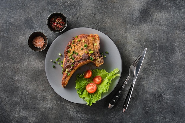 Chuleta de cerdo a la parrilla en un plato gris espolvoreado con cebollas verdes con ensalada y tomates cherry