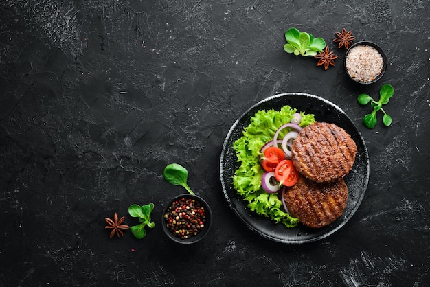 Chuleta frita para hamburguesa con verduras. En un plato negro sobre un fondo de madera Vista superior. Espacio libre para su texto. endecha plana