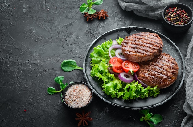 Chuleta frita para hamburguesa con verduras. En un plato negro sobre un fondo de madera Vista superior. Espacio libre para su texto. endecha plana