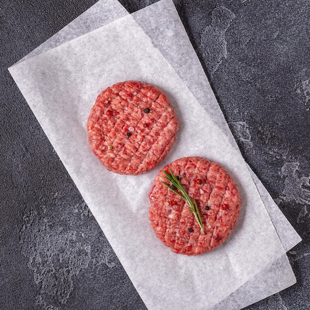 Foto chuleta de hamburguesa de carne cruda fresca con hierbas y especias en el tablero de piedra negra