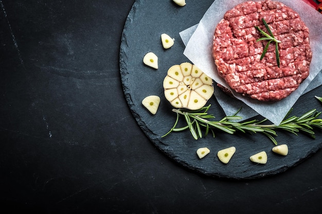 Chuleta de hamburguesa cruda de carne de res con ajo y romero sobre fondo negro con copia espacio top vi