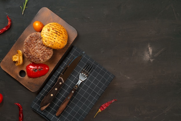 Chuleta de hamburguesa a la parrilla con un bollo sobre tabla de madera, vista superior