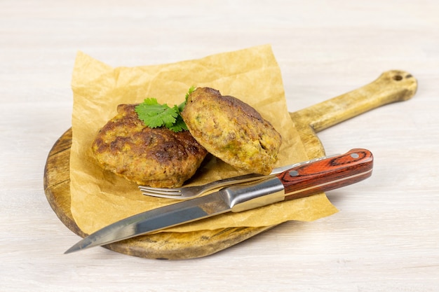 Chuleta de hamburguesas de carne de res de carne casera en tabla de cortar en blanco tablewith cuchillo y hierbas. Concepto de dieta baja en carbohidratos. De cerca. Enfoque selectivo. Copia espacio