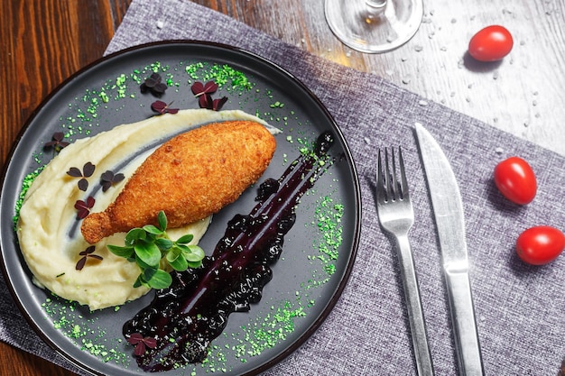 Foto chuleta de pollo kiev con puré de patatas en un plato de crutones y una copa de vino oscuro y de mal humor